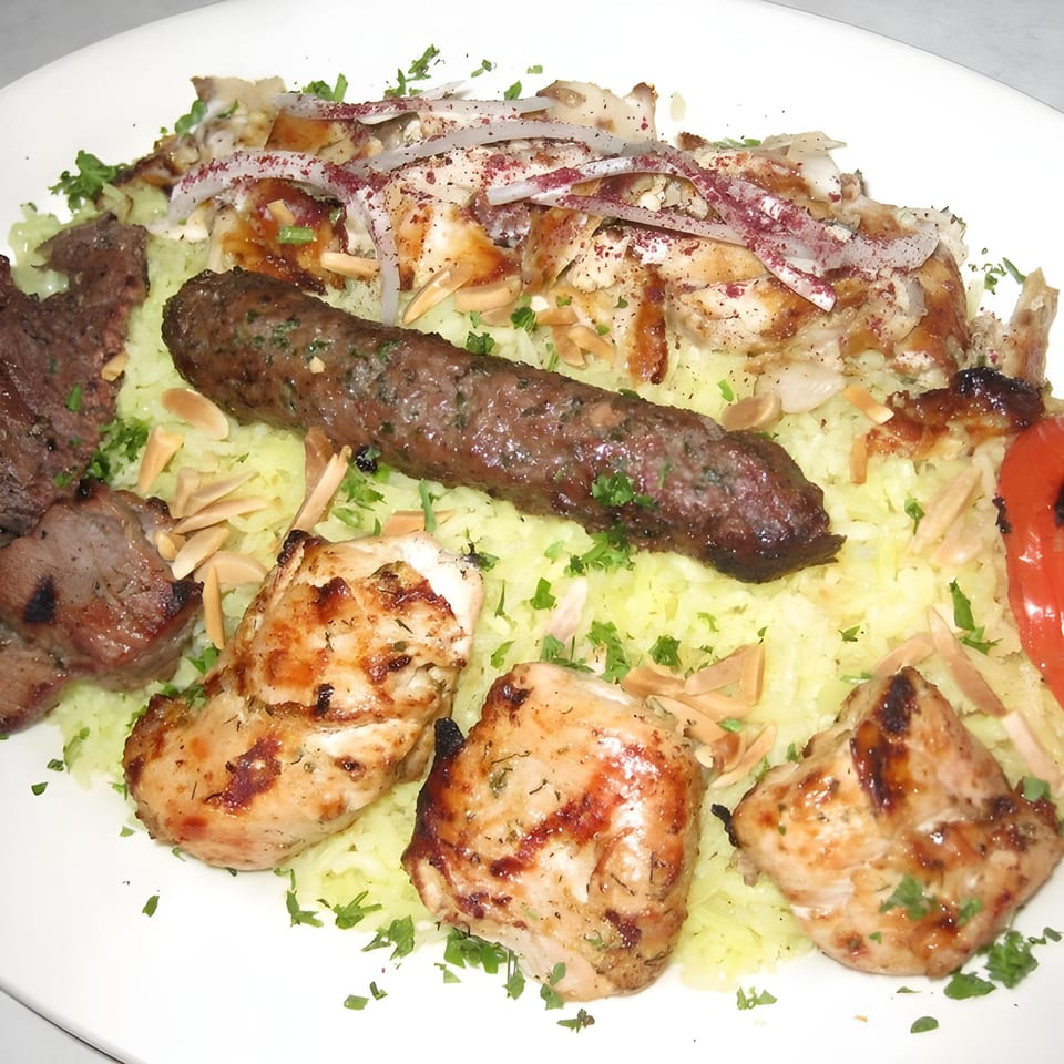 A Mediterranean mixed grill platter with various meats, rice, onions, and parsley on a white plate.
